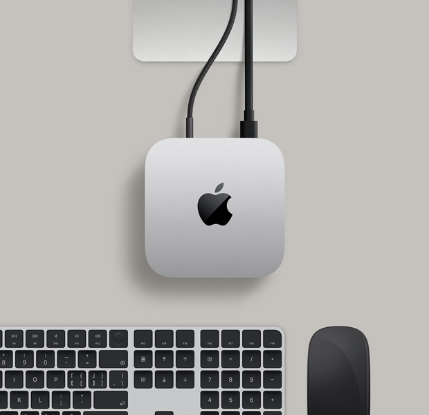 银色 Mac mini 的俯视图，两条插入背面端口的连接线连接至一台显示器，旁边有黑色妙控鼠标和黑色妙控键盘。