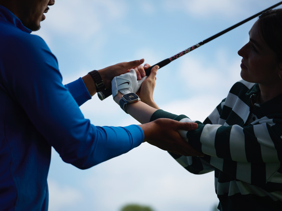 一名高尔夫教练正在帮助佩戴 Apple Watch 的高尔夫球手练习挥杆动作。