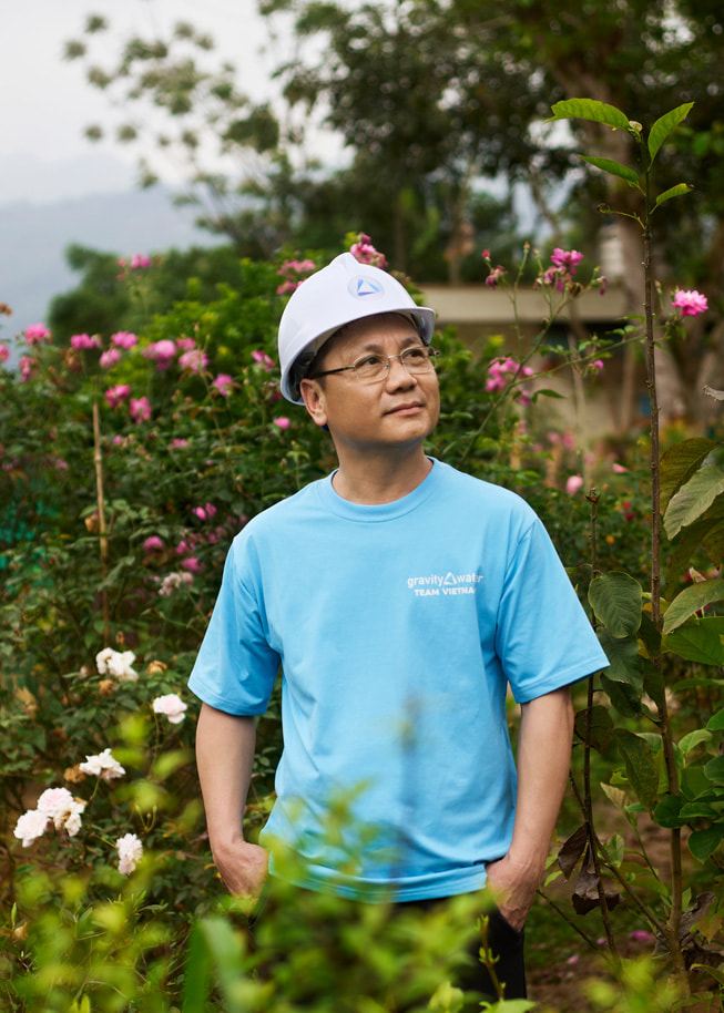Phan Viet Dung 头戴安全帽站在室外，身后有许多花朵。