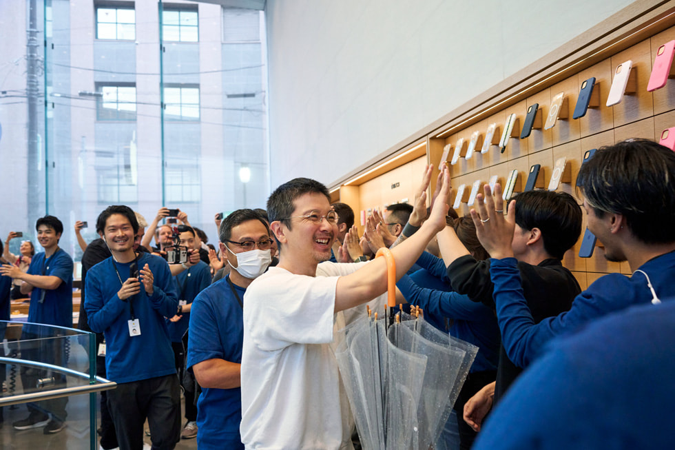 Apple 表参道零售店内，一位顾客与列队的 Apple 团队成员击掌。
