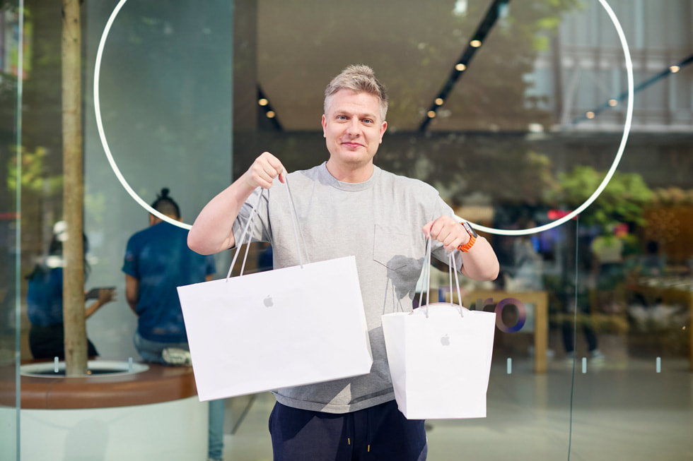 一位顾客举着两只 Apple 购物袋，里面装着他新购买的产品。