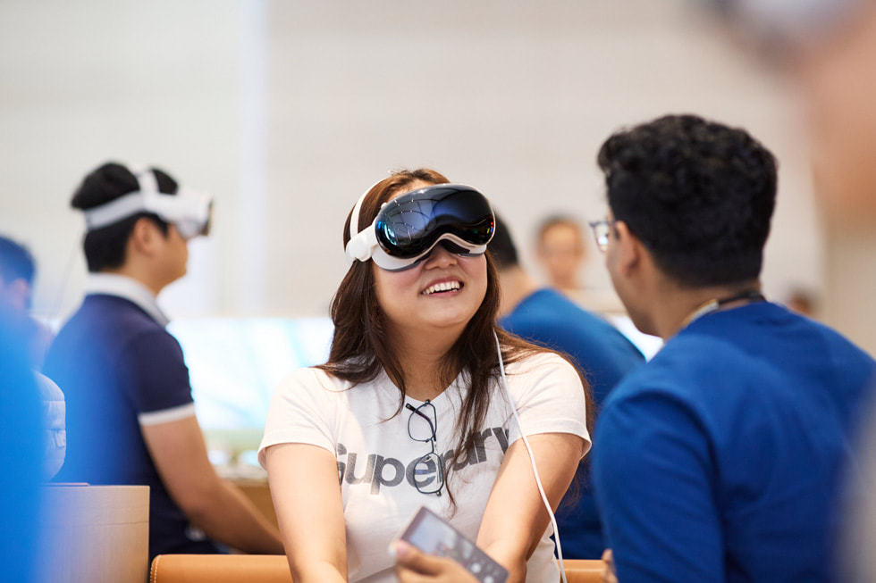 一位佩戴 Apple Vision Pro 的顾客微笑着与坐在身旁的团队成员说话。