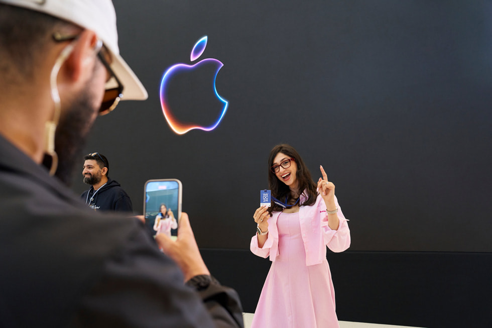 一位参与者摆姿势展示 WWDC24 参会证，一位 Apple 团队成员为其拍照。 