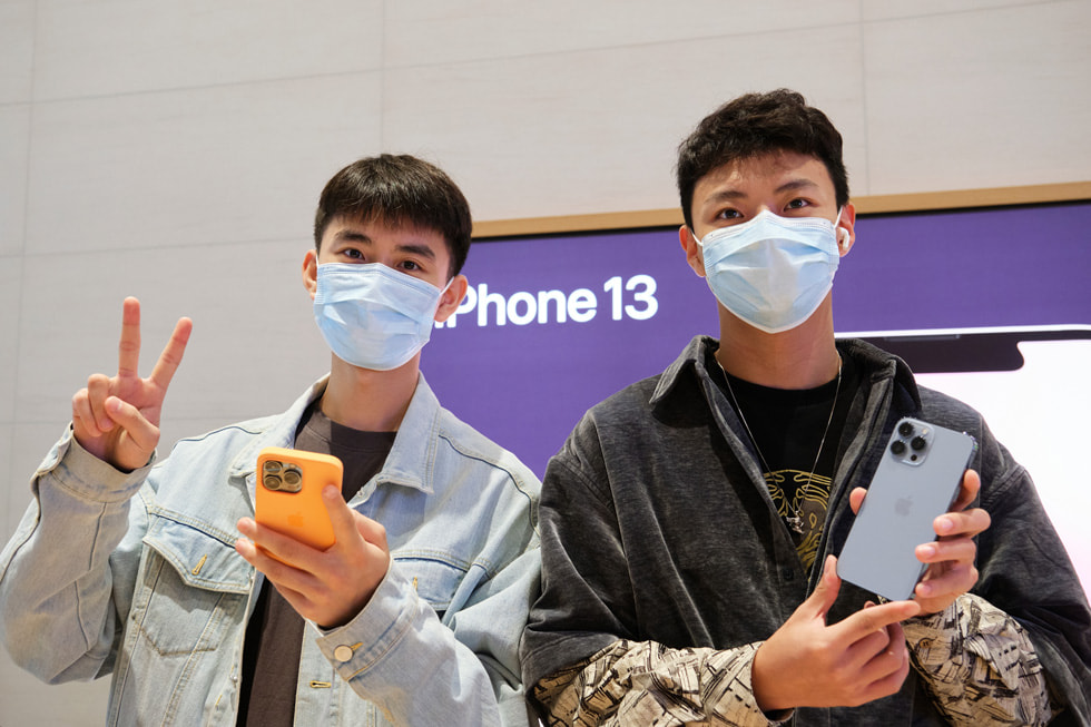 Apple 三里屯零售店内，一名与友人共同前来的顾客正在体验新款远峰蓝色 iPhone 13 Pro。
