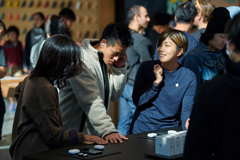 东京 Apple 表参道店内，顾客在 Apple 团队的帮助下试戴 AirPods Pro。