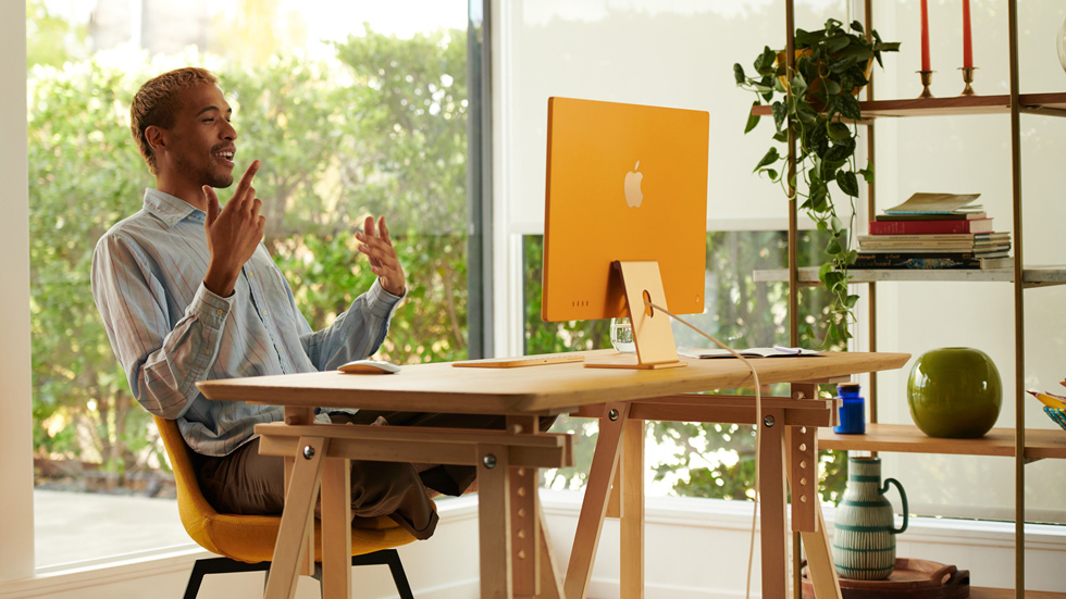 一名男性在家庭办公室里使用橙色的新款 iMac。