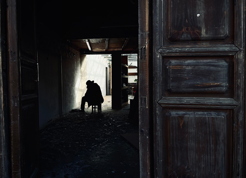 一扇敞开的门外，一个人影坐在碎片和阴影中。