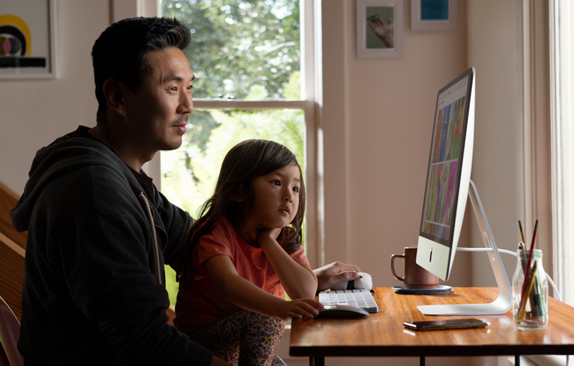 一对父女在家中的 iMac 上浏览照片。